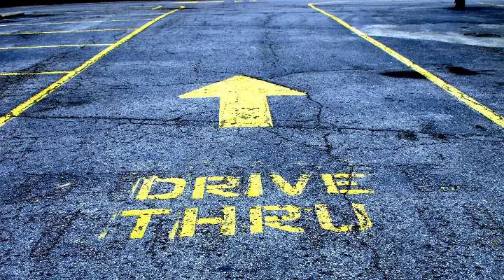 Photo of a drive through parking lot - Although the case could be made that fast food is one of the biggest contributors to the poor health and obesity epidemic throughout the US and much of the developed world, by using fast food paleo options as our guide, we look at healthy, whole food options within the sea of fast food junk to help you reconsile paleo eating out fast food with trying to be healthy. Although not a comprehensive list, these paleo fast food restaurants and paleo fast food lunch places will make your work lunches easier to deal with. Take a look at these 11 place on our paleo fast food list to get a sense of what is available.